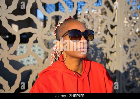 Wunderschöne Aufnahme einer schwarzen erwachsenen Frau, die eine schwarze Sonnenbrille trägt und für eine Kamera posiert Stockfoto