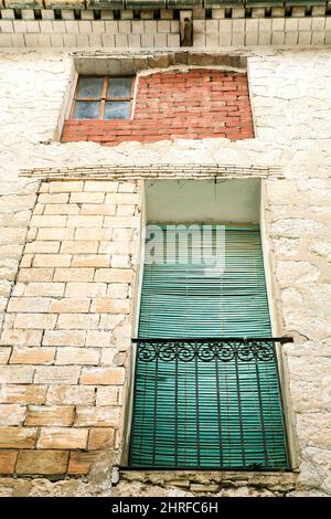 Alte Hausfassade mit rostigem Balkon und grünem Blind in Guadalest, Alicante, Spanien. Stockfoto