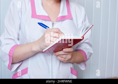 Arzt oder Krankenschwester hält ein Notizbuch in der Hand und schreibt dort. Stockfoto