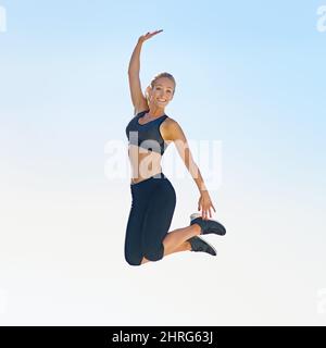 Es fühlt sich gut an, fit zu sein. Ganzkörperaufnahme einer sportlichen jungen Frau, die gegen einen blauen Himmel springt. Stockfoto