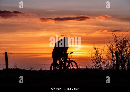 Brighton, Großbritannien. 25.. Februar 2022. Brighton, 25. 2022. Februar: Ein Radfahrer beobachtet den Sonnenuntergang vom Devil's Dyke aus, im South Downs National Park, nördlich von Brighton.Quelle: Andrew Hasson/Alamy Live News Stockfoto