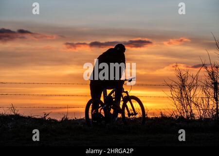 Brighton, Großbritannien. 25.. Februar 2022. Brighton, 25. 2022. Februar: Ein Radfahrer beobachtet den Sonnenuntergang vom Devil's Dyke aus, im South Downs National Park, nördlich von Brighton.Quelle: Andrew Hasson/Alamy Live News Stockfoto