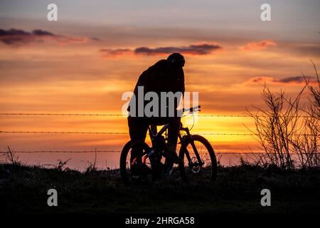 Brighton, Großbritannien. 25.. Februar 2022. Brighton, 25. 2022. Februar: Ein Radfahrer beobachtet den Sonnenuntergang vom Devil's Dyke aus, im South Downs National Park, nördlich von Brighton.Quelle: Andrew Hasson/Alamy Live News Stockfoto