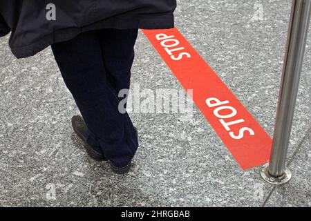 Eine Person, die an einer roten Stopplinie steht, die für einen sozialen Distanzierungszweck auf den Boden geschrieben wurde Stockfoto
