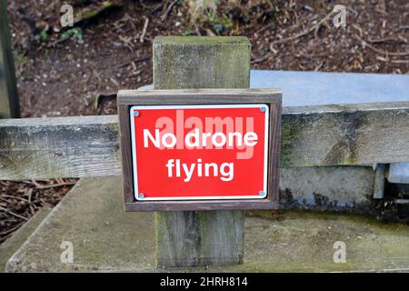 Ein rechteckiges No Drone fliegendes Schild mit weißem Schriftzug auf einem roten Hintergrund, das an einem Holzzaun befestigt ist Stockfoto