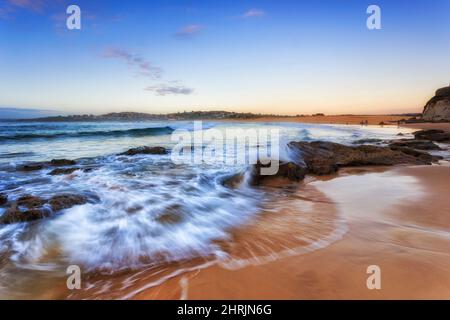 Sandsteinfelsen und Felsbrocken auf dem Sand des Curl Curl Beach von Sydney North Shore bei Sonnenaufgang. Stockfoto