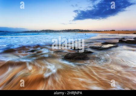 Einfallende unscharfe Welle auf Felsen und Felsbrocken des Curl Curl Beach Sydney North Shore of pacific bei Sonnenaufgang. Stockfoto