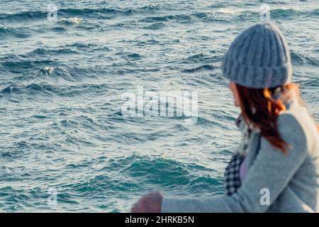 Eine unkenntlich unfokussiere Frau blickt mit Wellen auf das Meer Stockfoto