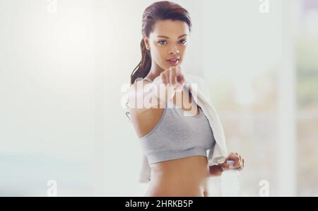 Beginnen Sie noch heute. Ein beschnittenes Porträt einer attraktiven jungen Frau, die während ihres Trainings zu Hause auf die Kamera zeigt. Stockfoto