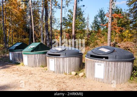 Reihe großer Recycling-Behälter in einem Recycling-Zentrum auf dem Land an einem sonnigen Herbsttag. Herbstfarben im Hintergrund. Stockfoto