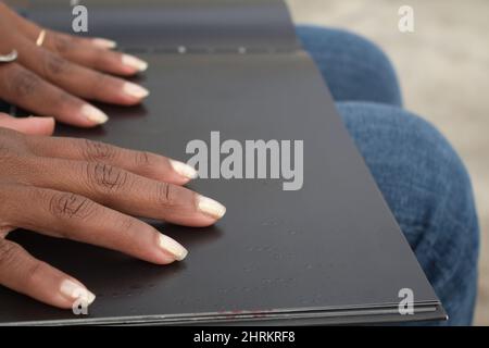 Nahaufnahme der Hände einer afroamerikanischen Frau, die in einem schwarzen Buch Braille liest Stockfoto