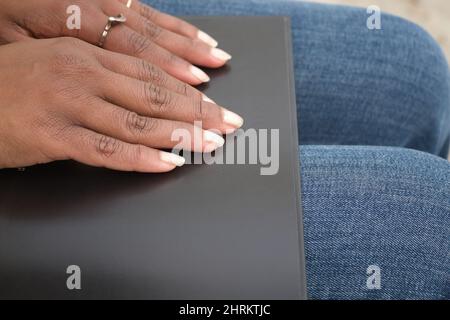 Nahaufnahme der Hände einer afroamerikanischen Frau, die in einem schwarzen Buch Braille liest Stockfoto