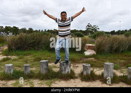 Junger Mann, der auf den Stumps im Park steht und lustige Posen macht. Stockfoto