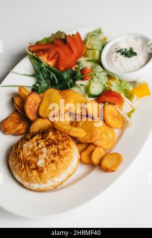 Draufsicht auf Käse mit gebratenen Kartoffeln und Gemüse auf einem großen weißen Keramikteller Stockfoto