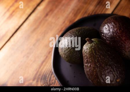 Mexikanische Avocado (Persea americana) auf rustikalem Holztisch. Hauptbestandteil zur Zubereitung von Guacamole. Nahaufnahme des Bildes mit Kopierbereich. Stockfoto