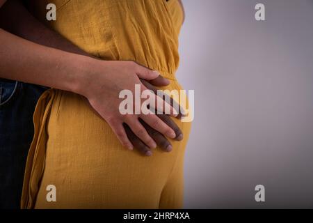 Nahaufnahme der Hände eines schwarzen Mannes, der den Bauch einer weißen Frau berührt, ist ein interrassisches Paar schwanger und erwartet ein Kind Stockfoto