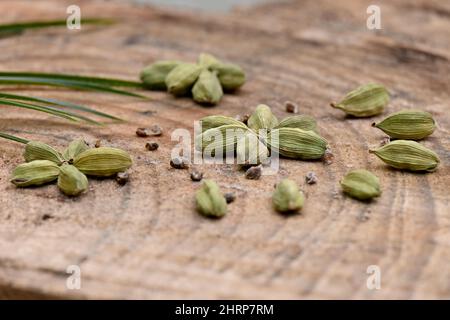 Selektive Fokusaufnahme eines Bündels von grünem reifem Kardamom mit grünen Blättern auf einem hölzernen Hintergrund. Stockfoto