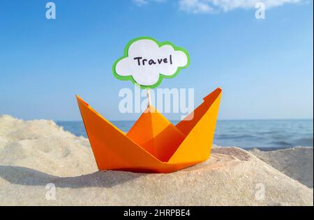 Orange kleines Papierboot auf Sandy Seashore auf dem Hintergrund Meer und sauberer blauer Himmel Nahaufnahme am sonnigen Sommertag. Halten Sie sich an den weißen grünen leeren Sprechbubl Stockfoto