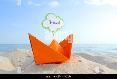 Orange kleines Papierboot auf Sandy Seashore auf dem Hintergrund Meer und sauberer blauer Himmel Nahaufnahme am sonnigen Sommertag. Halten Sie sich an den weißen grünen leeren Sprechbubl Stockfoto