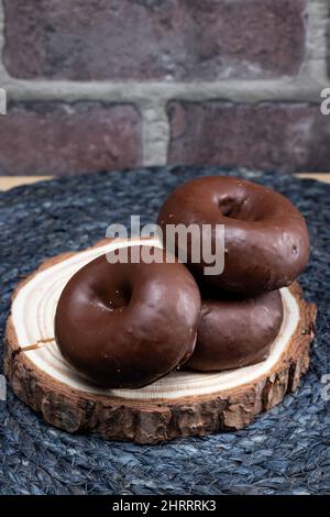 Die vertikale Aufnahme des Stapels der schokoladenüberzogenen Donuts auf dem Holzteller Stockfoto