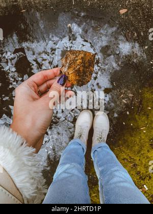 In einem hohen Winkel ein Mädchen, das ein trockenes Herbstblatt in der Hand hält und auf einer Pfütze steht Stockfoto