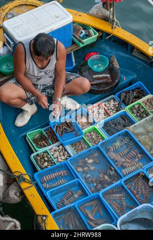 Ein lokaler Fischer verkauft den Fang von einem kleinen Boot an der Ufermauer von Sai Kung in Hongkong Stockfoto