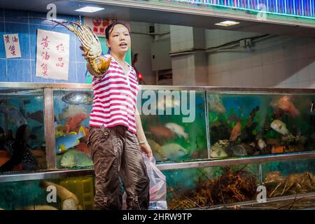 Ein Mitarbeiter zeigt einen von einem Kunden ausgewählten Hummer aus Meeresfrüchten in Tanks vor einem Restaurant im Sai Kung Waterfront, Hongkong Stockfoto