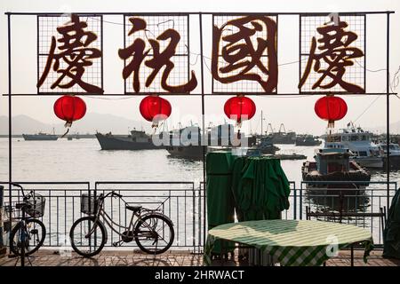 Chinesisches Schild („Celebrate National Day“) und traditionelle rote Laternen an der Uferpromenade von Cheung Chau, einer abgelegenen Insel Hongkongs Stockfoto