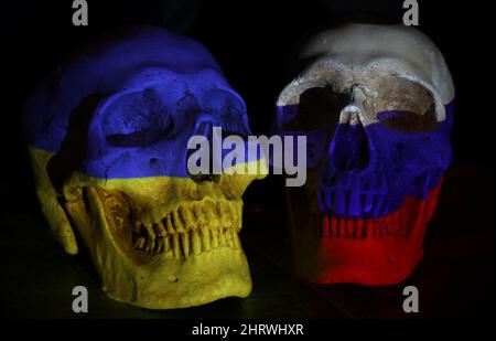 Zwei gegenüberliegende Schädel, die mit den Nationalflaggen Russlands und der Ukraine auf einer abgedunkelten Karte der Region und einem schwarzen Hintergrund bemalt sind. Die w Stockfoto