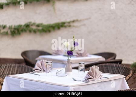 Leere Gläser und Blumen in einem neuen Luxusrestaurant mit überdachten Tischen Stockfoto