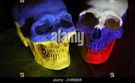 Zwei gegenüberliegende Schädel, die mit den Nationalflaggen Russlands und der Ukraine auf einer abgedunkelten Karte der Region und einem schwarzen Hintergrund bemalt sind. Die w Stockfoto