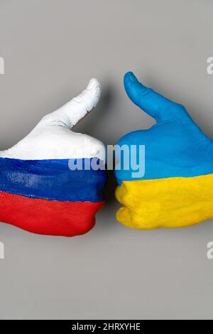 Hände, die in die Flaggen der Ukraine und Russlands gemalt sind, heben einen Finger auf einen grauen Hintergrund. Vertikal. Daumen nach oben Hand der Hände mit der Zeichnung einer Flagge Stockfoto