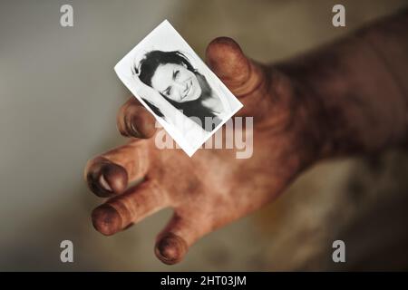 Wo ist sie jetzt? Eine schmutzige Hand, die ein schwarz-weißes Bild einer schönen Frau hält. Stockfoto