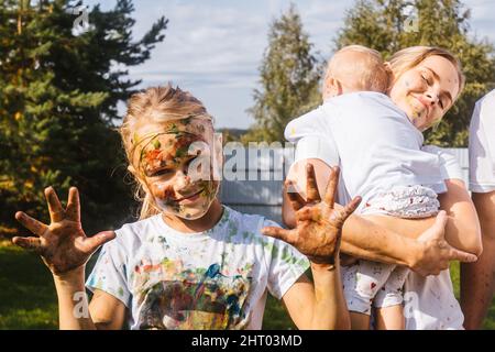 Nahaufnahme Porträt des kleinen Mädchens. Mädchen ist gebeizt Aquarelle, Spaß Freizeitaktivitäten im Garten. Mutter und Schwester und Hintergrund. Stockfoto