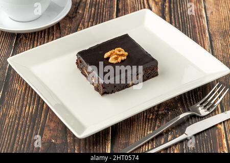 Nussbaum und dunkler Schokoladenbrownie auf einem weißen Porzellanteller auf einem Holztisch Stockfoto
