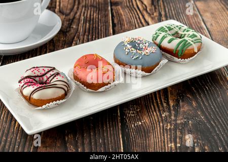 Leckere bunte Mini-Donuts mit Kaffee auf Holztisch Stockfoto