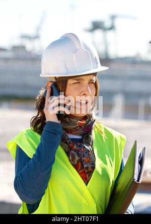 Die Lösung der Baubedürfnisse. Eine Bauarbeiterin, die am Telefon spricht. Stockfoto