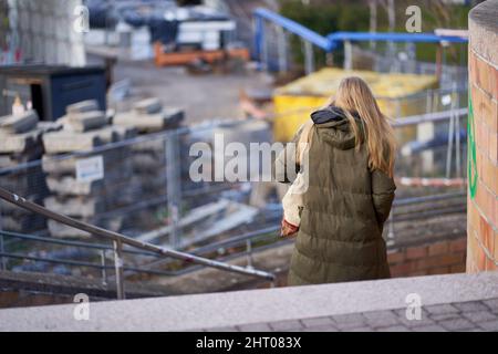 Stuttgart, 06. Januar 2022: Junge Frau in Winterkleidung geht die Stufen hinunter. Baustellenbahnprojekt Stuttgart 21. Stockfoto