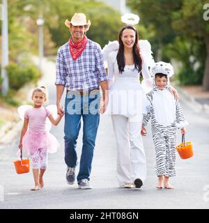 Diese Kollektion von Outfits ist unschlagbar. In voller Länge aufgenommen, wie eine Familie in ihren Halloween-Kostümen die Straße entlang läuft. Stockfoto