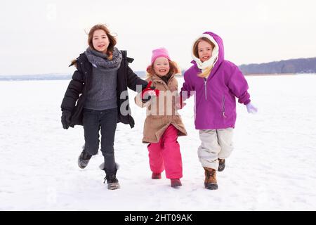 Lasst uns Schneeengel machen. Drei junge Schwestern, die draußen im Schnee Rennen. Stockfoto