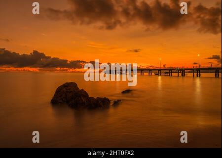 Spektakulärer, lebhafter, rot-oranger Sonnenaufgang über Palm Cove mit Austern verkrusteten Felswänden im Vordergrund, die das Interesse an dem legendären Pier in QLD, Australien, wecken. Stockfoto