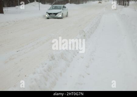 Straße im Winter. Schneeverwehung auf der Strecke. Das Auto fährt im Schneesturm auf einer schneebedeckten Straße entlang. Die Autobahn ist mit Schnee bedeckt. Stockfoto