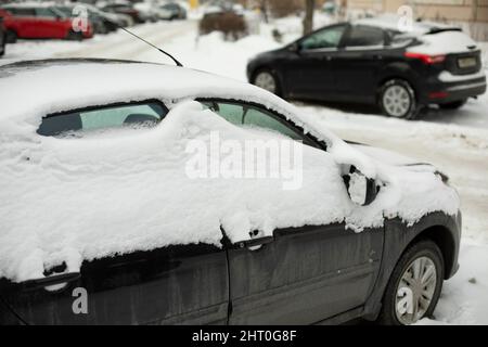 Das Auto hat auf dem Parkplatz gefroren. Ansicht Transportseite. Das Auto ist mit Eis bedeckt. Schneeschicht auf dem Auto. Stockfoto