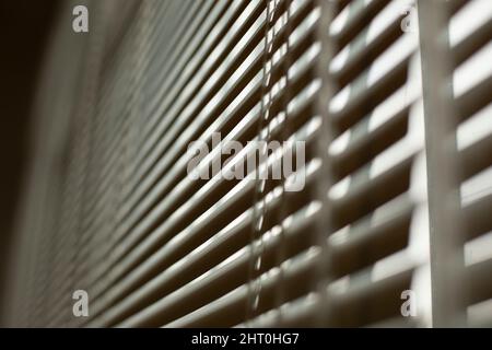 Jalousien am Fenster. Weiße Jalousien bedecken das Fenster vor der Sonne. Details zur Innenausstattung. Diagonal aufnehmen. Stockfoto