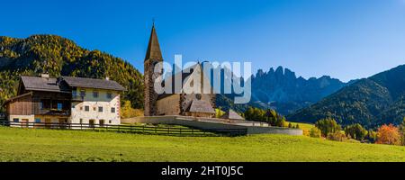 Panoramablick auf die Kirche St. Magdalena im Villnösstal, Nordwände und Gipfel der Geisler-Gruppe in der Ferne, im Herbst. Stockfoto