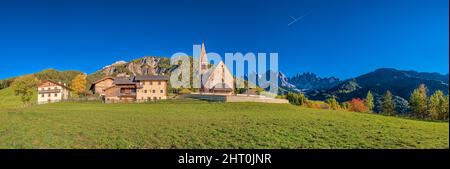 Panoramablick auf die Kirche St. Magdalena im Villnösstal, Nordwände und Gipfel der Geisler-Gruppe in der Ferne, im Herbst. Stockfoto