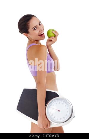 Ihre Essgewohnheiten zu ändern, bedeutet Gewichtsverlust. Studioaufnahme einer attraktiven jungen Frau in Turnkleidung mit Apfel- und Waage. Stockfoto