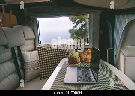 Reise-Lifestyle und digitaler Online-Nomadenarbeitsplatz im modernen Wohnmobil. Laptop-Computer auf dem Tisch und Natur außerhalb des Fensters. Roaming Stockfoto