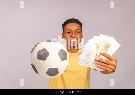 Sportwette, Gambing und Lifestyle-Konzept für die ganze Familie. Aufgeregt afroamerikanischen jungen Kerl genießen ihren Sieg, stehen mit Fußball und viel Stockfoto