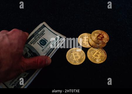 Nahaufnahme eines Mannes, der Dollarscheine mit Bitcoins auf dunklem Hintergrund hält Stockfoto